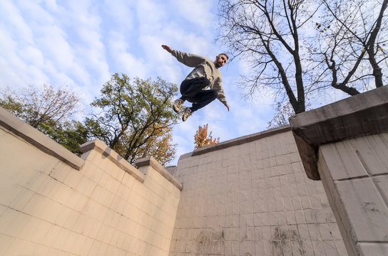 A young guy performs a jump through the space between the concrete parapets. The athlete practices parkour, training in street conditions. The concept of sports subcultures among youth
