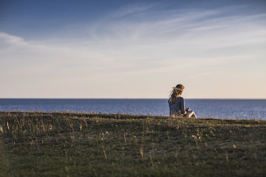 Woman sitting by the sea at sunset
