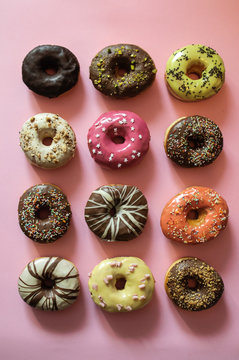 Twelve colorful donuts on the pink background