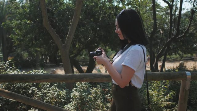 Beautiful young tourist brunette woman takes photos of nature in Barcelona park on small professional digital camera. Travel concept. Dolly shot, 4k.