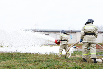 Firefighters extinguish the fire with a chemical foam coming from the fire engine through a hose