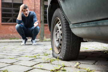 Crouched Man Pointing At Punctured Car Tire © Andrey Popov