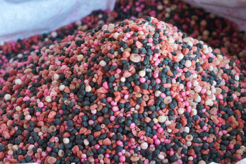 a heap of red fertilizer over white fertilizer bag. Nitrogen (N): leaf growth,Phosphorus (P): Development of roots,Potassium (K): Strong stem growth