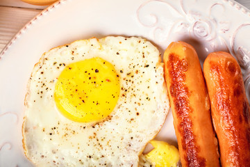Breakfast of sunny side up eggs, fried sausages on white round plate, close up.