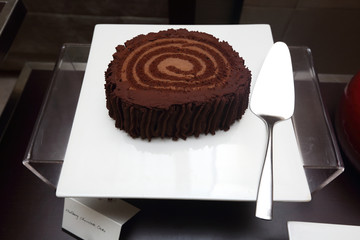 Mulberry Chocolate Cake Big Roll Cream in Catering White Dish with silver cake spatula, Grand Dessert Buffet in Luxury Restaurant Hotel
