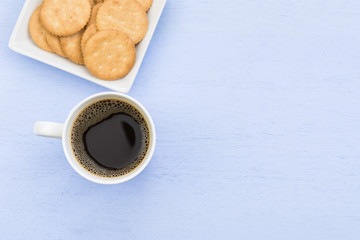 cup of coffee and cracker in a dish on light blue wooden board with copy space for text, top view.
