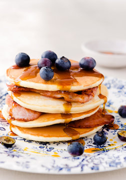 Stack of pancakes layered with bacon, blueberries and maple syru