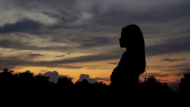 Silhouette of woman looking up at sunset sky with wind blowing hair
