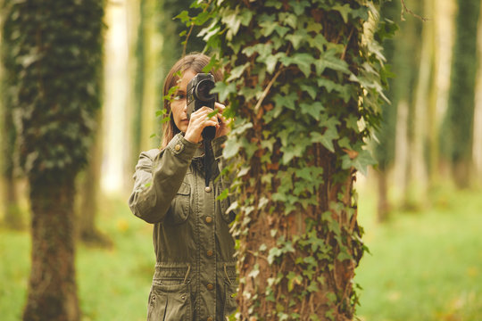 Woman with film camera is behind a tree. Autumnal forest.