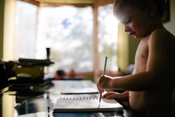 little boy drawing on a notebook with a pencil at home