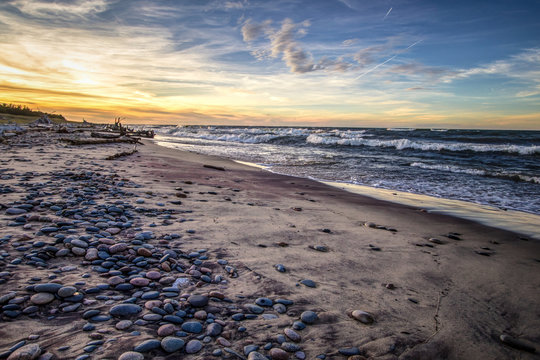 Scenic Windy Beach Sunset Background. Wide sandy beach with waves crashing on the shore at Whitefish Point on the coast of Lake Superior. Wide angle with rocks in foreground and waves at the horizon.