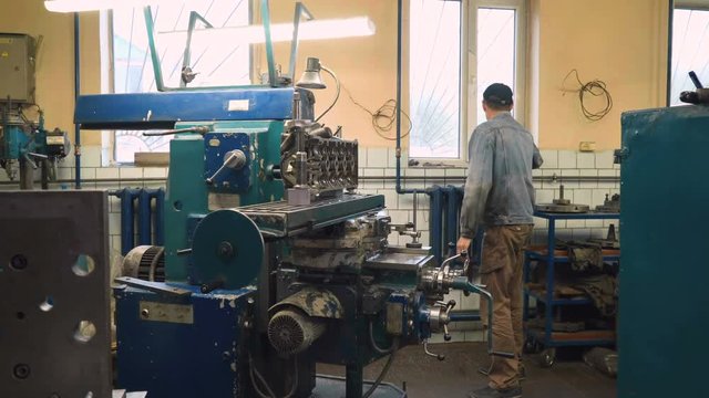 Mature caucasian man waiting for milling of cylinder head on milling machine in old shabby car service, cleaning hands with towel. Shot with Sony a7s and Atomos Ninja Flame, slide.