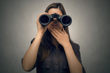 Business woman looking through binoculars closing her mouth with her hand and being shocked by what she saw.