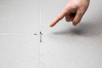 Man's hand finger pointing to space between tiles. Damaged tiles seam. Building problem concept.