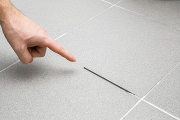 Man's hand finger pointing to space between tiles. Damaged tiles seam. Building problem concept. - obrazy, fototapety, plakaty