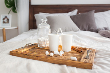 Fototapeta na wymiar Two mugs on a tray white bed with a cinnamon stick, breakfast concept