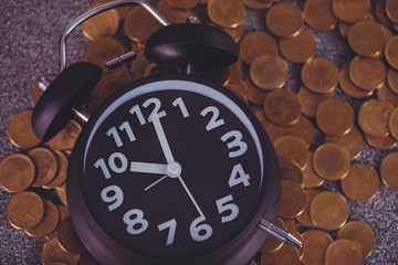 Alarm clock and piles of coin on working table, time for savings money concept. vintage tone.