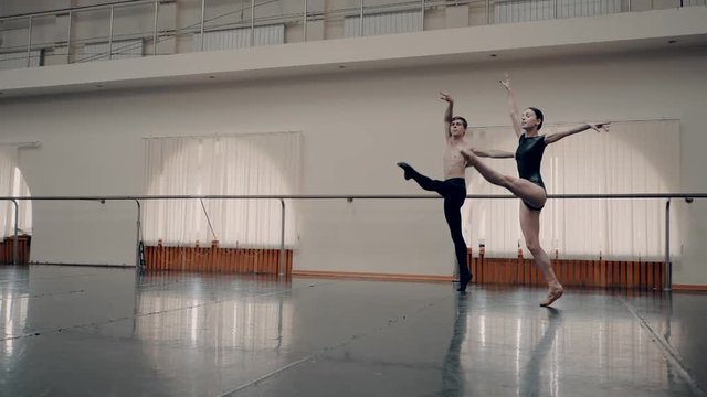 Young man practicing in classical ballet with young beautiful woman in black clothing in the gym. Minimalism interior, sensual dance. Slow motion. adagio