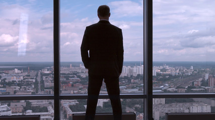Fototapeta na wymiar Full length back view of successful businessman in suit standing in office with hands on waist, CEO. Businessman from the back in front of a city view on the window