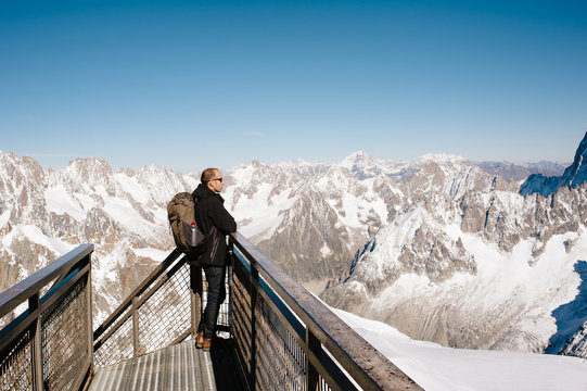 Man standing on a walkway at Aiguille du Midi looking at the Mont Blanc Massif mountains
