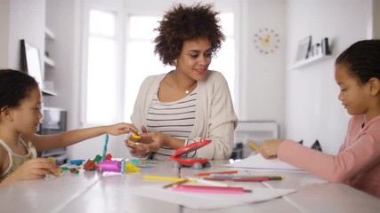 Wide shot of a young mother or child minder with kids at the table having fun playing and drawing