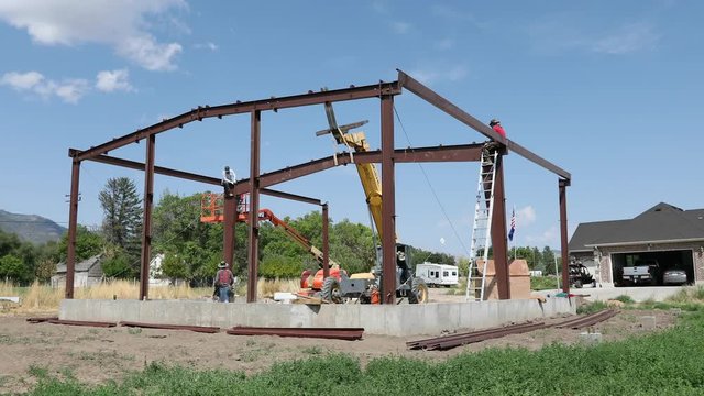 Construction men building steel farm building. Construction of rural farm agriculture building. Delivery and installation of prefabricated metal building. Engineering architectural design.