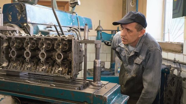 Mature caucasian man watching how cutter processes surface of cylinder head, using milling machine in old shabby car service. Shot with Sony a7s and Atomos Ninja Flame.