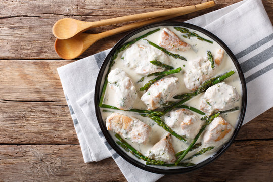 Pieces of chicken with baby asparagus in a creamy sauce close-up on a plate. horizontal top view