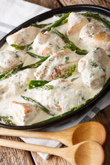 sliced chicken with baby asparagus in cream sauce close-up on the table. vertical
