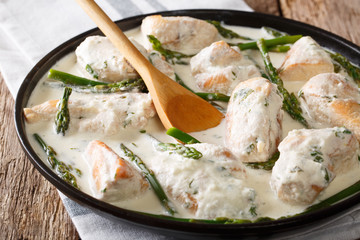 Chicken fillet with asparagus in a creamy sauce close-up on a plate. horizontal