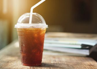 Cold iced black coffee with book on wooden table background.