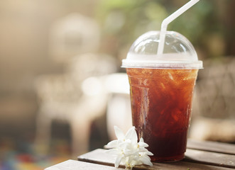 Cold iced black coffee with flower on wooden table in the garden background.