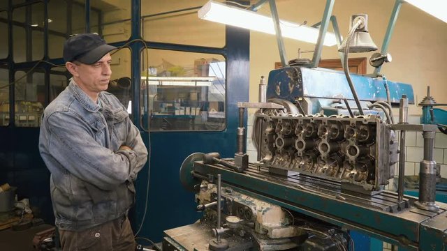 Mature caucasian man watching how cutter processes surface of cylinder head, using milling machine in old shabby car service. Shot with Sony a7s and Atomos Ninja Flame.