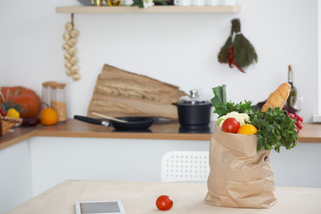 Paper bag full of vegetables on the table in kitchen interiors. Healthy meal and vegetarian concept