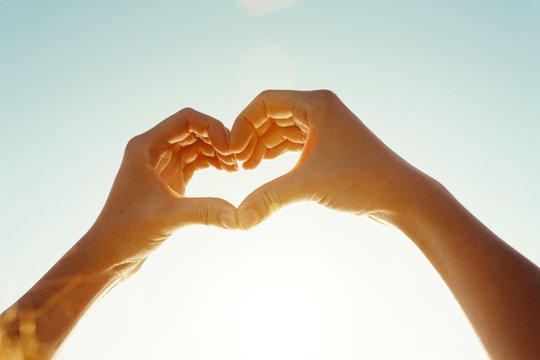 Close-up of woman's hand makes a heart shape against the sky