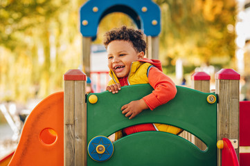 Adorable little 1-2 year old toddler boy having fun on playground, child wearing orange hoody jacket and yellow vest - Powered by Adobe