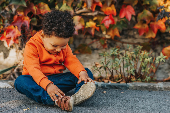 Portrait of adorable african toddler boy playing outdoors on a nice autumn day, wearing bright orange hoody jacket