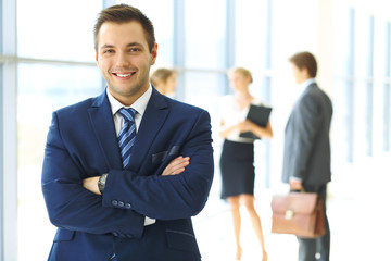 Fototapeta premium Smiling businessman in office with colleagues in the background