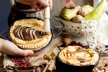 pie with pear and nuts in a frying pan. woman smears a tassel and honey pie