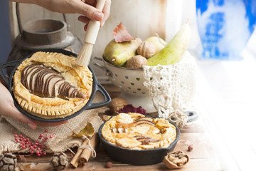 pie with pear and nuts in a frying pan. woman smears a tassel and honey pie
