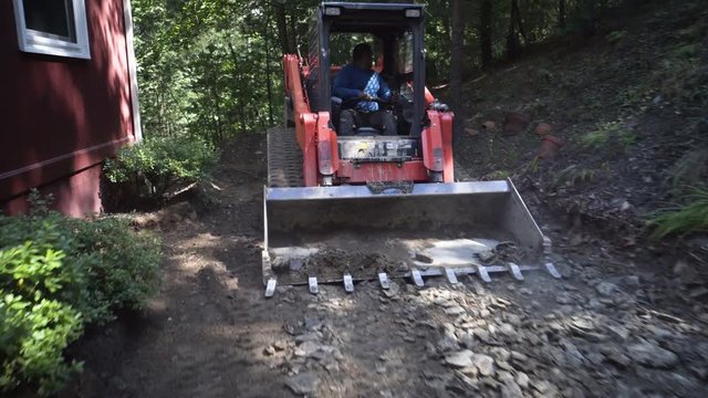 Kubota track skid steer smooths out the stones and dirt excavating for landscaping and hardscaping.