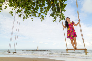 Asia women on wooden swing seat hanging on nice clean beach and deep blue sky