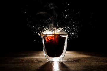 Hot and aromatic coffee spilling from transparent glass cup