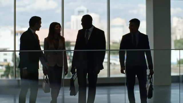 Silhouettes of business team discussing something in hall of modern office building with panoramic windows
