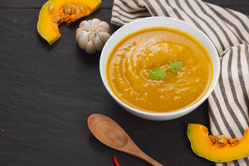 Pumpkin soup in a bowl with fresh pumpkins, garlic and parsley herbs