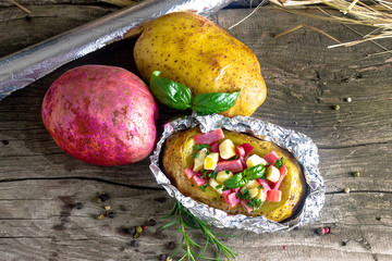 baked potato in foil with ham and cheese on a wooden background