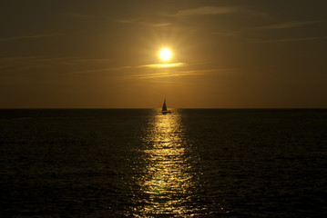 Fototapeta premium sunset or sunrise over the sea horizon, the sunny path and the silhouette of a sailboat