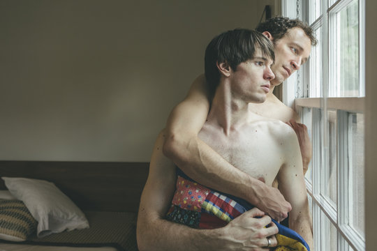 Embracing Gay Men Couple with Blanket Looking Out their Bedroom Window