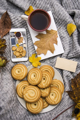 woman's bed top view on a lazy sunday morning in cold weather . Lifestyle with mobile phone, book, cakes, autumn colorful leaves and warm clothes.