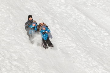 A family of four with the twins slide down a snow hill in winter in the Park